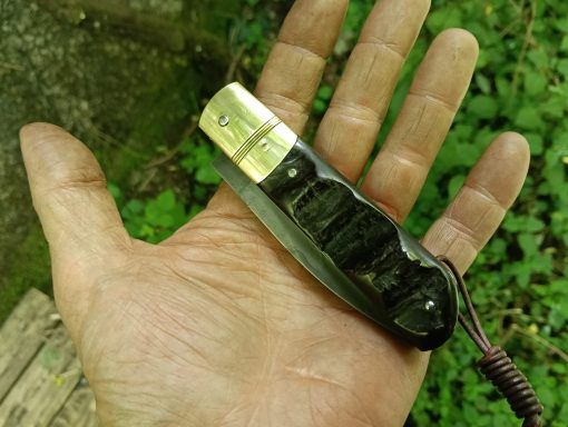 Couteau pliant en main, avec une poignée sombre et une lame légèrement visible.