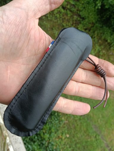 Étui noir tenu dans une main avec une cordelette, en extérieur.