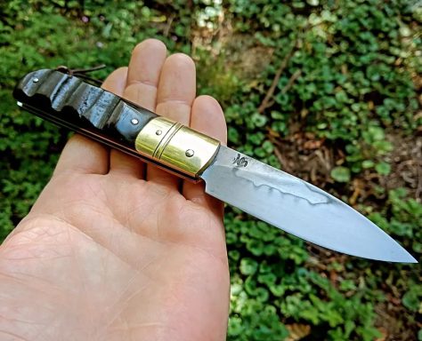 Couteau pliant tenu dans une main, lame en acier brillante et manche en bois.