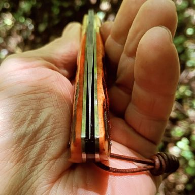 Couteau pliant en bois, tenu à la main, avec une lanière attachée.