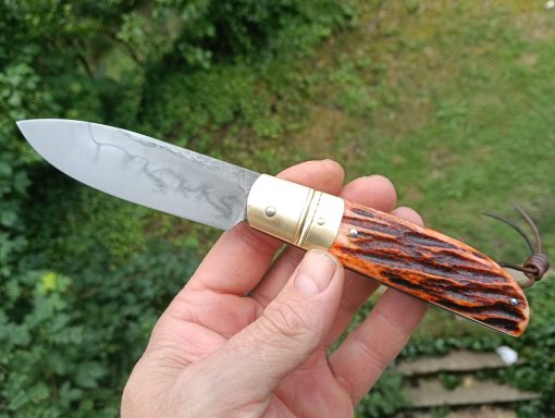 Couteau pliant avec une lame en acier et un manche en bois clair et foncé.