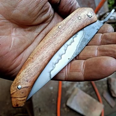 Couteau pliant avec une lame en métal et un manche en bois, posé dans une main.
