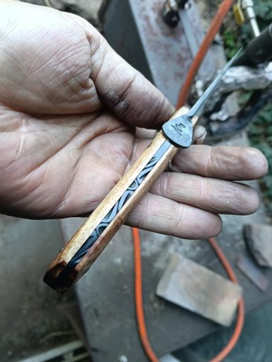 Main dans un environnement de travail, tenant un outil en métal avec un manche en bois.