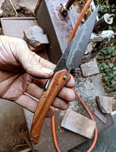 Un couteau avec une lame en métal et un manche en bois, tenu par une main.