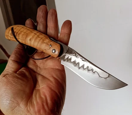 Couteau pliant avec une lame dentelée, tenu dans une main. Poignée en bois.